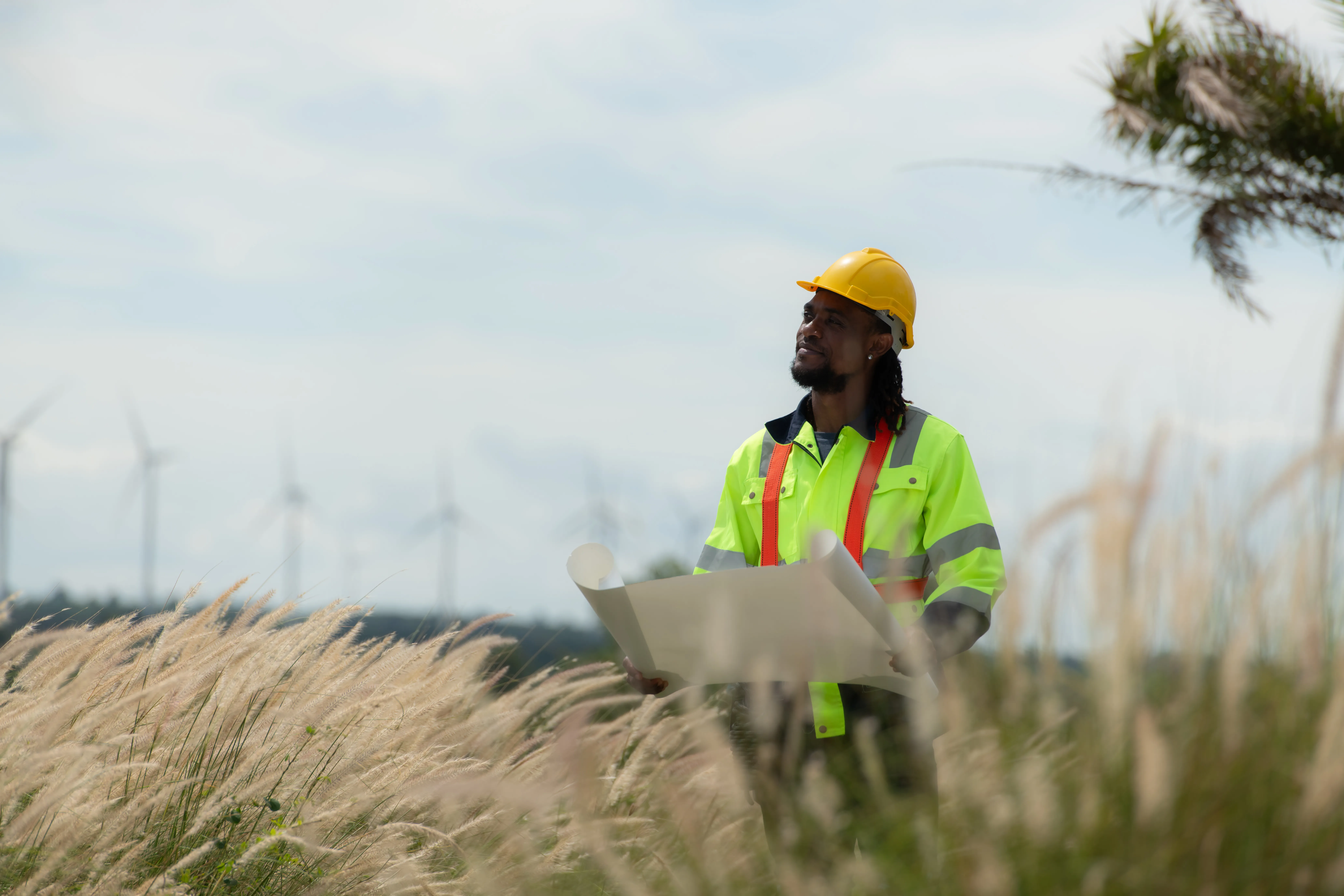 Front view of an engineer wearing a safety vest and a yellow helmet while standing in a field